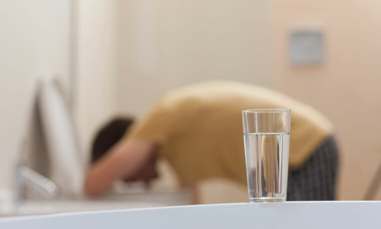 person böjer sig över toalettstol, vattenglas i förgrunden
