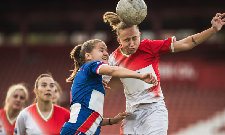 Två unga kvinnor hoppar upp för att nicka samma boll