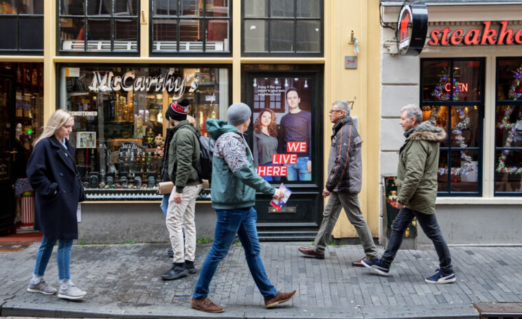 männsikor på gågata, passerar skyltfönster med en familj på bild