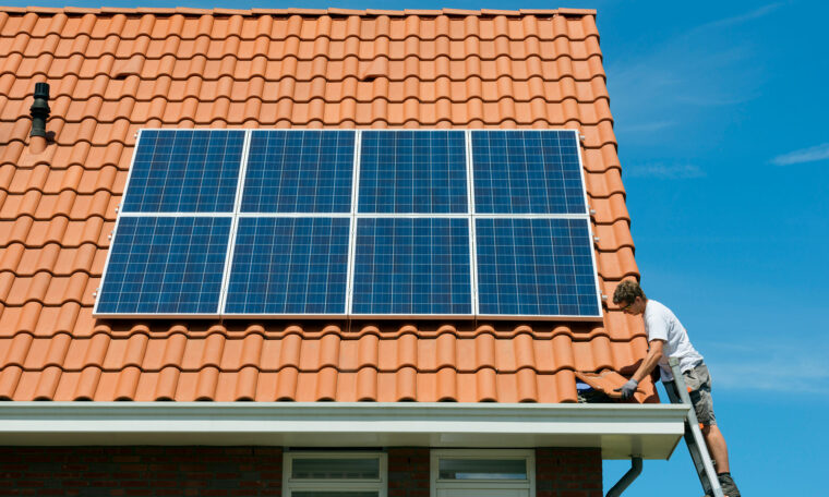 Man på stege kontrollerar solceller på villatak