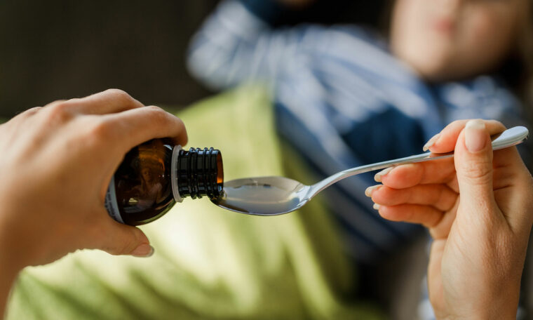 någon häller upp medicin på en sked till ett barn