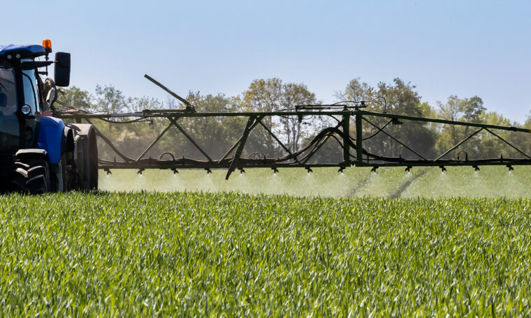 traktor på fält besprutar grödorna