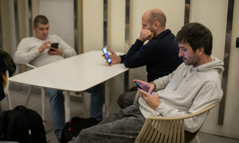 Tre män sitter vid ett bord och tittar på sina mobiler medan de ignorerar varandra.