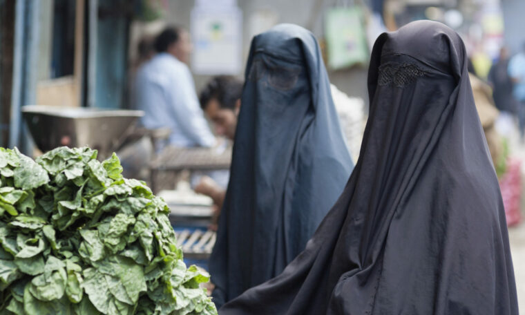 Två kvinnor i burka handlar grönsaker.