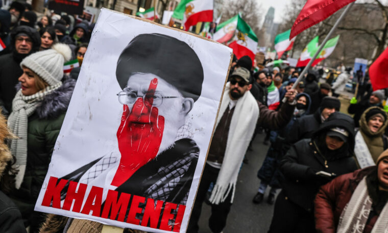 Demonstranter håller upp bild på ayatolla Khamenei med en hand som pekar finger målad över hans ansikte.